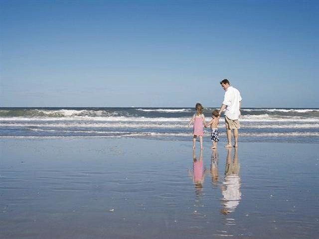 A man and a child walking on the beach near the ocean.