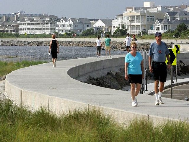 People walking along a curved waterfront pathway on a sunny day.